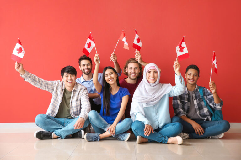 Group,Of,Students,With,Canadian,Flags,Sitting,Near,Color,Wall